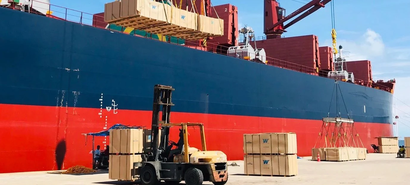 MDF cargo being loaded onto a bulk vessel, with a forklift and stacked cargo on the quay